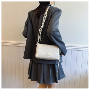 Detail view of cream pillow bag with textured fabric and woven rope shoulder strap