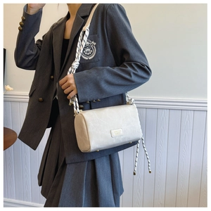 Detail of cream cylindrical crossbody bag with black and white rope strap and gold hardware