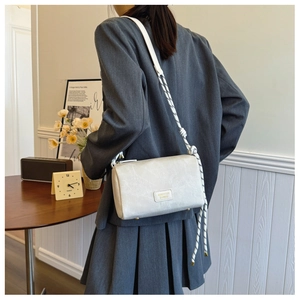 Close-up of cream rectangular shoulder bag featuring unique black and white rope strap