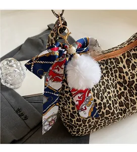 Détail d'un sac cabas léopard avec un nœud décoratif en ruban et un pendentif pompon doux