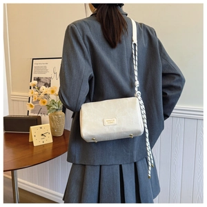Detail of white textured shoulder bag with rope strap and metal protective feet on base