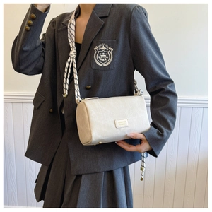 Detail of cream pillow bag featuring woven rope strap and branded metal plaque logo