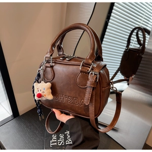 Détail du sac Boston en simili cuir marron foncé avec logo embossé et breloque en peluche