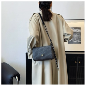 Detail of crossbody bag with black woven rope strap on a trench coat model