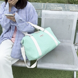 Close-up of a mint green pleated travel bag with detachable strap in outdoor setting