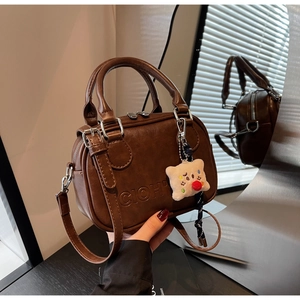 Détail du sac Boston en cuir marron foncé avec logo gaufré et breloque en peluche blanche