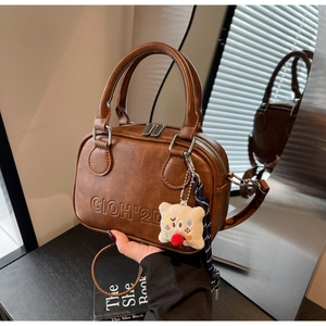 Détail d'un sac bandoulière marron vintage avec logo embossé et pendentif ours en peluche
