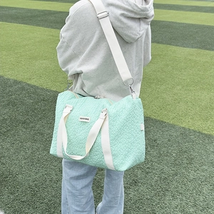 Close-up of mint green travel bag with rhombus texture and fashion label on grass