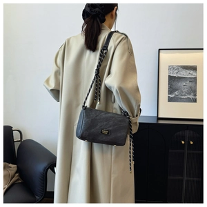 Detail of dark gray pillow bag featuring a decorative woven rope strap on a model