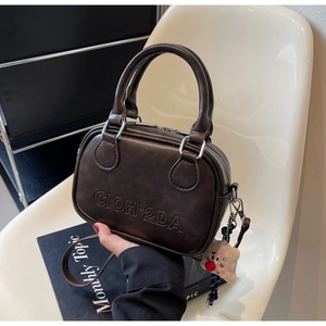 Détail d'un sac Boston marron foncé avec lettrage embossé et breloque ours sur une chaise