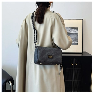 Detail of dark grey cylindrical shoulder bag with woven strap and gold rivets