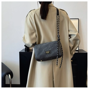 Detail of gray envelope shoulder bag with woven rope strap on beige trench coat