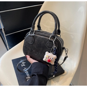 Détail d'un sac bandoulière noir vintage avec lettres embossées et un pendentif d'ours