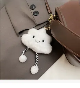 Close-up of a white plush cloud charm with embroidery on a dark leather handbag