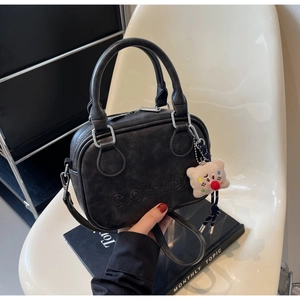Sac à main vintage noir mat avec logo embossé et breloque ours en peluche sur chaise blanche