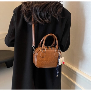 Détail du sac bandoulière vintage marron caramel avec logo embossé et breloque peluche