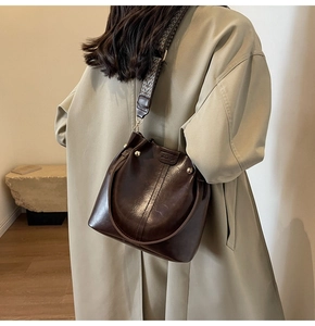 Detail of dark brown glossy bucket bag with wide geometric strap and metal studs