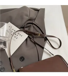 Detail of adjustable long leather strap and golden metal buckle on brown shoulder bag