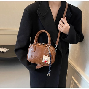 Sac Boston marron vintage avec logo embossé et pendentif en peluche porté par un mannequin