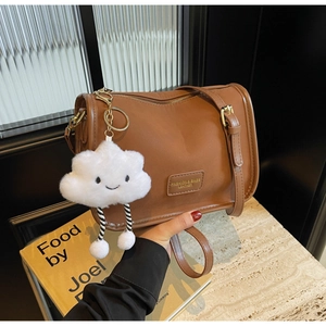Detailed shot of brown leather shoulder bag with white plush cloud charm and gold zipper
