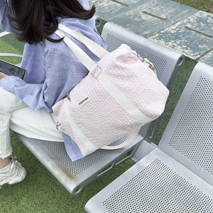 Detail of light pink quilted travel bag with white straps and fashion bag label outdoor
