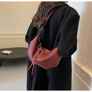 Detail showing burgundy pleated croissant bag with wide strap and silver chain accessory