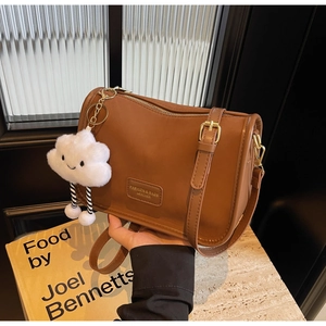 Close-up of brown leather shoulder bag with cute white cloud plush pendant and gold buckle