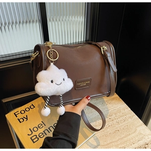 Detail of dark brown leather pillow bag featuring a metal logo and white cloud plush charm