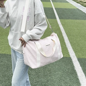 Pink quilted travel bag with white handles and shoulder strap shown on a green lawn