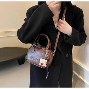 Vue détaillée du sac à bandoulière vintage marron avec lettrage embossé et breloque ours