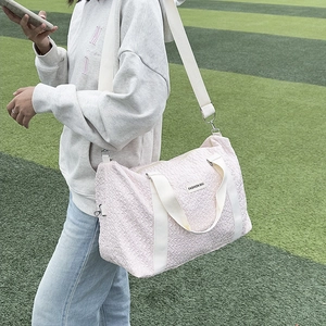 Pink textured travel bag with white handles shown in use at an outdoor sports track