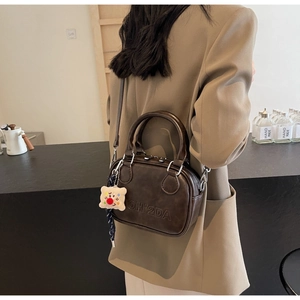 Détail du sac vintage en cuir marron avec lettres embossées et charm en peluche