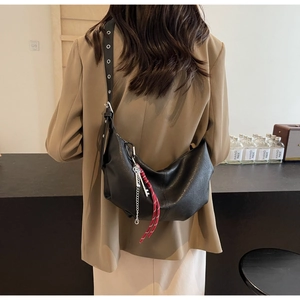 Detail of black crescent crossbody bag featuring red cord and metal chain accessories