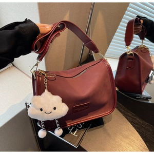 Detailed view of a dark red leather shoulder bag with plush cloud charm and logo patch