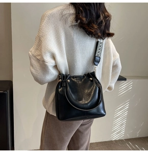Close-up of black leather bucket bag with geometric wide strap on model shoulder