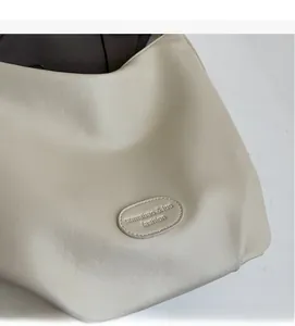 Gros plan détaillé sur la texture du cuir crème et le logo embossé du sac cabas