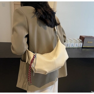 Detail of a beige ruched crossbody bag with red woven rope and metal chain accents