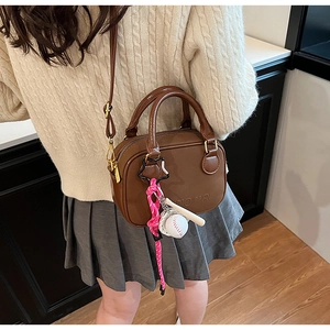 Détail d'un mini sac bowling en cuir marron avec gaufrage OUTDOOR et breloque baseball