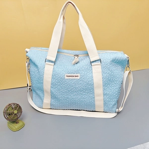 Close-up of light blue travel bag with ripple texture, woven handles and tassel detail