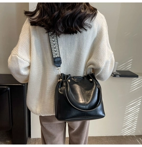 Detail of black pleated leather bucket bag with geometric strap on a model shoulder