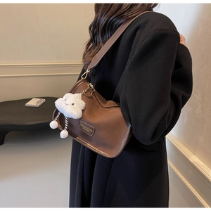 Detailed shot of brown shoulder bag with leather patch and plush white charm