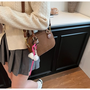 Detail of brown leather handbag featuring gold hardware and a pink baseball charm