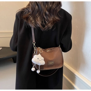 Detail of dark brown crossbody bag with cloud plush charm on a black blazer model