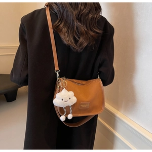 Detailed close-up of brown leather pillow bag featuring a plush cloud charm and logo patch