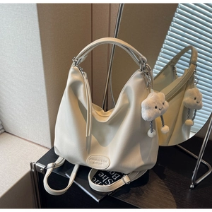 Détail du sac hobo en cuir crème avec un charm nuage en peluche et de longues tirettes