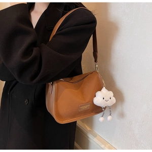 Close-up of brown leather crossbody bag with wide strap and cloud plush charm