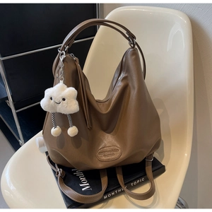 Détail d'un sac hobo marron avec breloque nuage posé sur une chaise en cuir chic