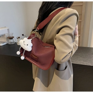 Detail of wine red leather underarm bag with wide strap and cloud plush pendant accessory