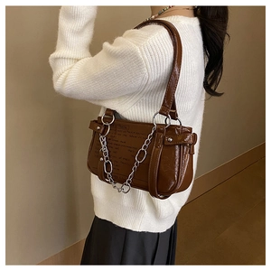 Close-up of a dark brown patent leather shoulder bag with silver chain and artistic text