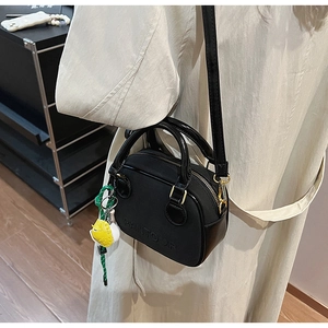 Close-up of minimalist black crossbody bag with logo embossing and yellow charm accessory